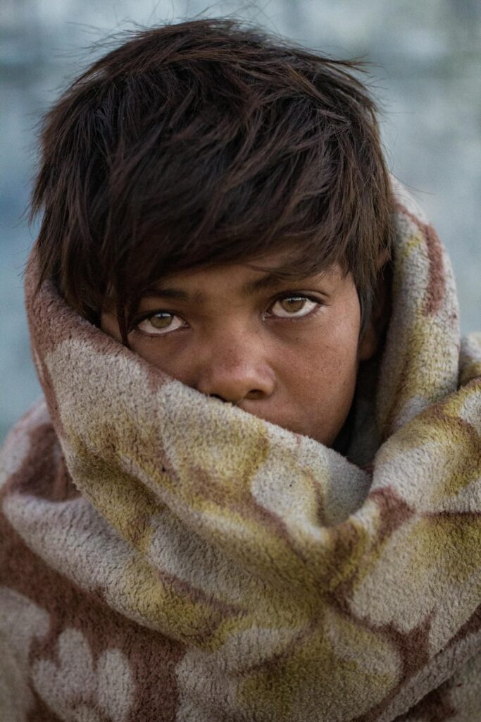 Boy with expressive eyes wrapped in blanket outdoors, showcasing innocence and warmth.